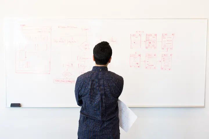 Mies katsoo valkotauluun kirjoitettuja muistiinpanoja. Kuvituskuva.