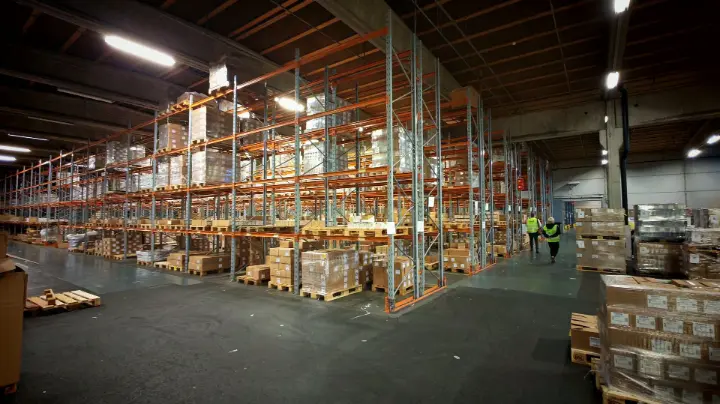 Kaksi työntekijää kävelee tehtaan varastotiloissa.